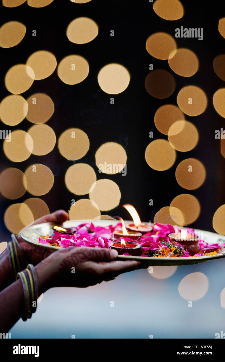 Close-up of a woman's hand holding oil lamps and Rose petals in a plate Stock Photo