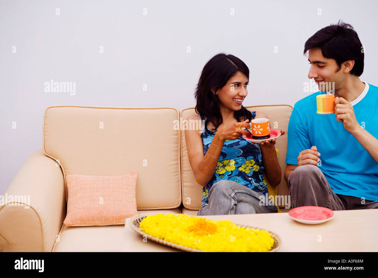 Young couple sitting on a couch and holding cups of tea Stock Photo - Alamy