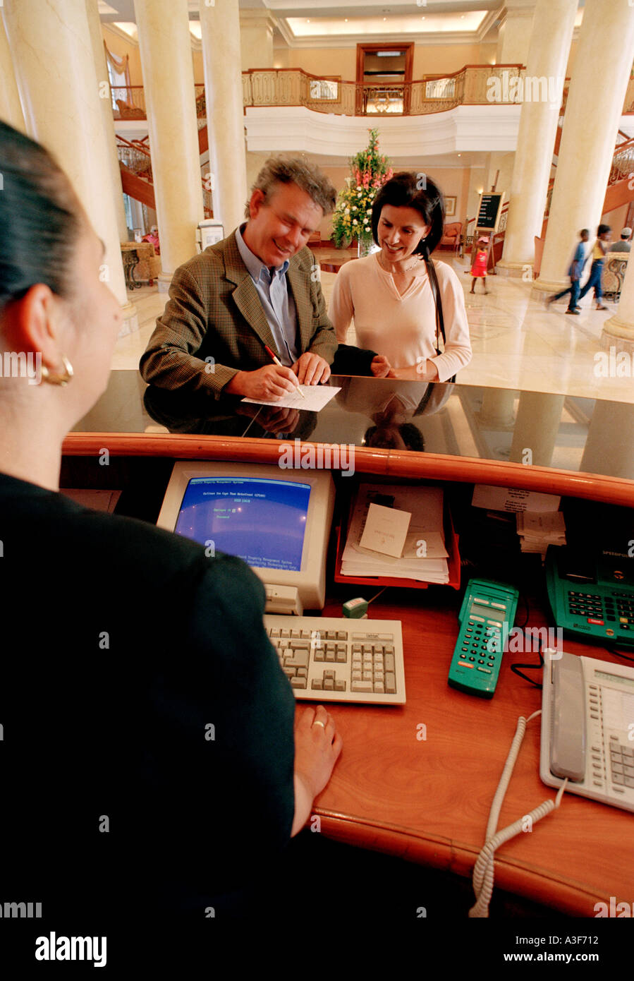 couple checking into hotel with receptionist in foreground Stock Photo