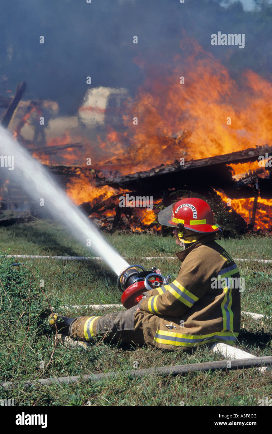 Volunteer Fireman Extinguishing Controlled Structure Fire as Practice Exercise With Ambulance Standing By in the Background Stock Photo