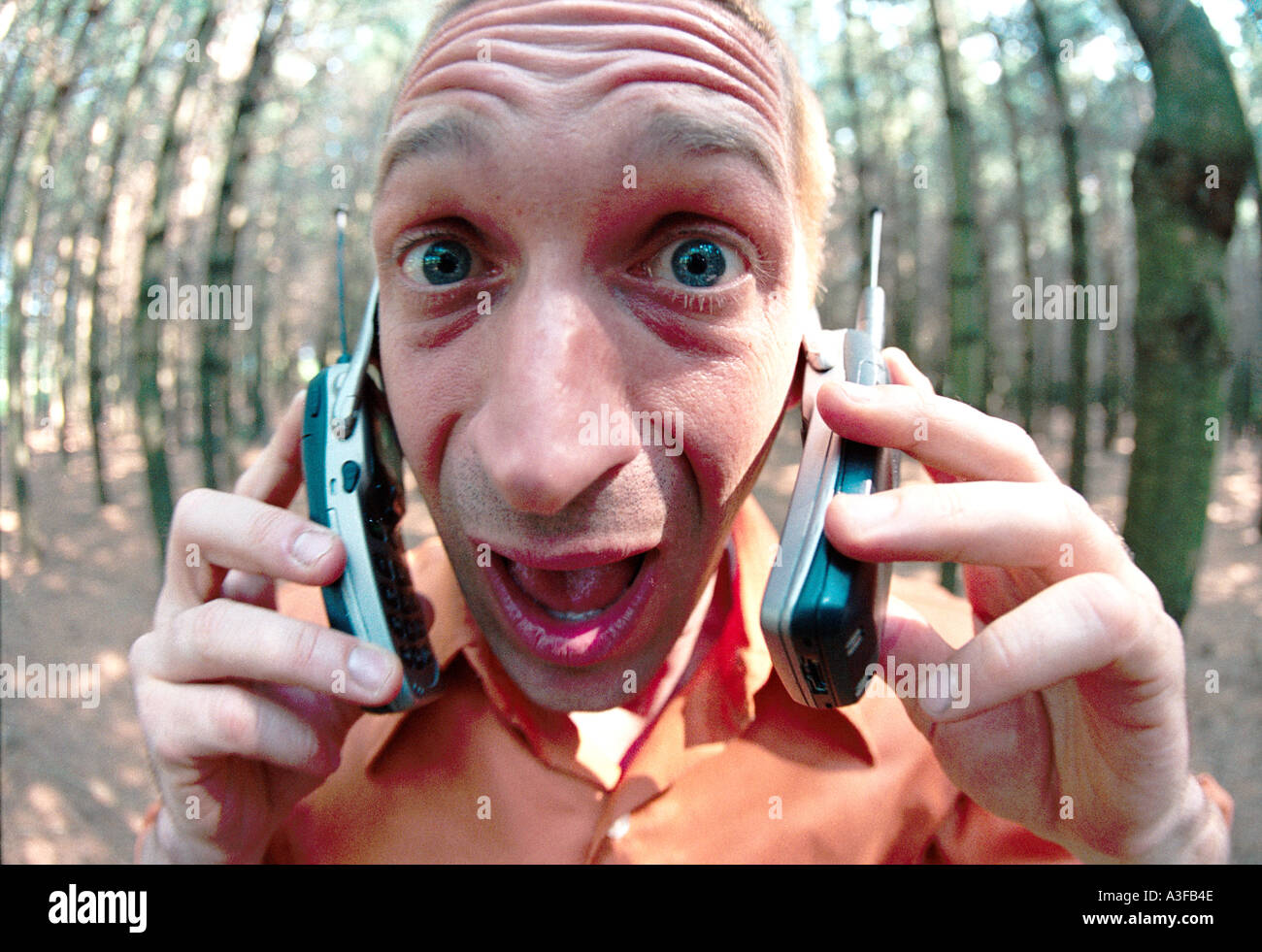 An excited man yells into two phones in the forest Stock Photo