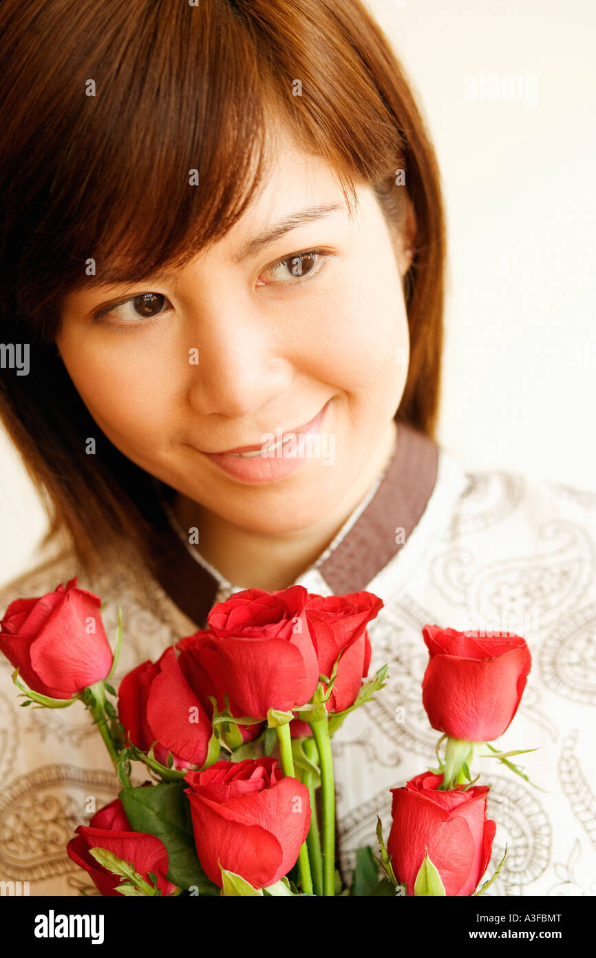 Close-up of a young woman smiling and holding a bouquet of red roses ...