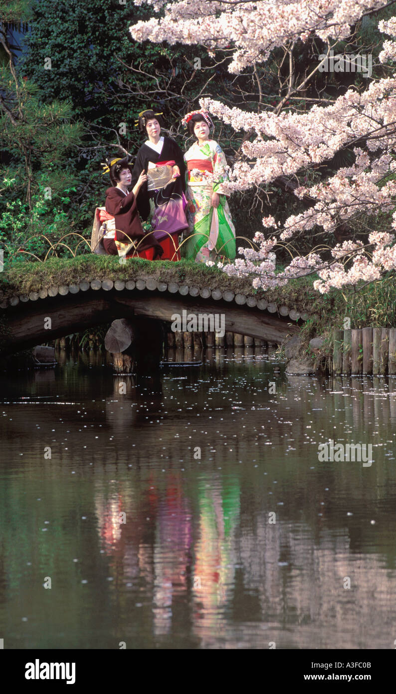 Geisha girls in colorful kimonos on bridge over pond reflecting cherry blossoms in Tokyo park Stock Photo