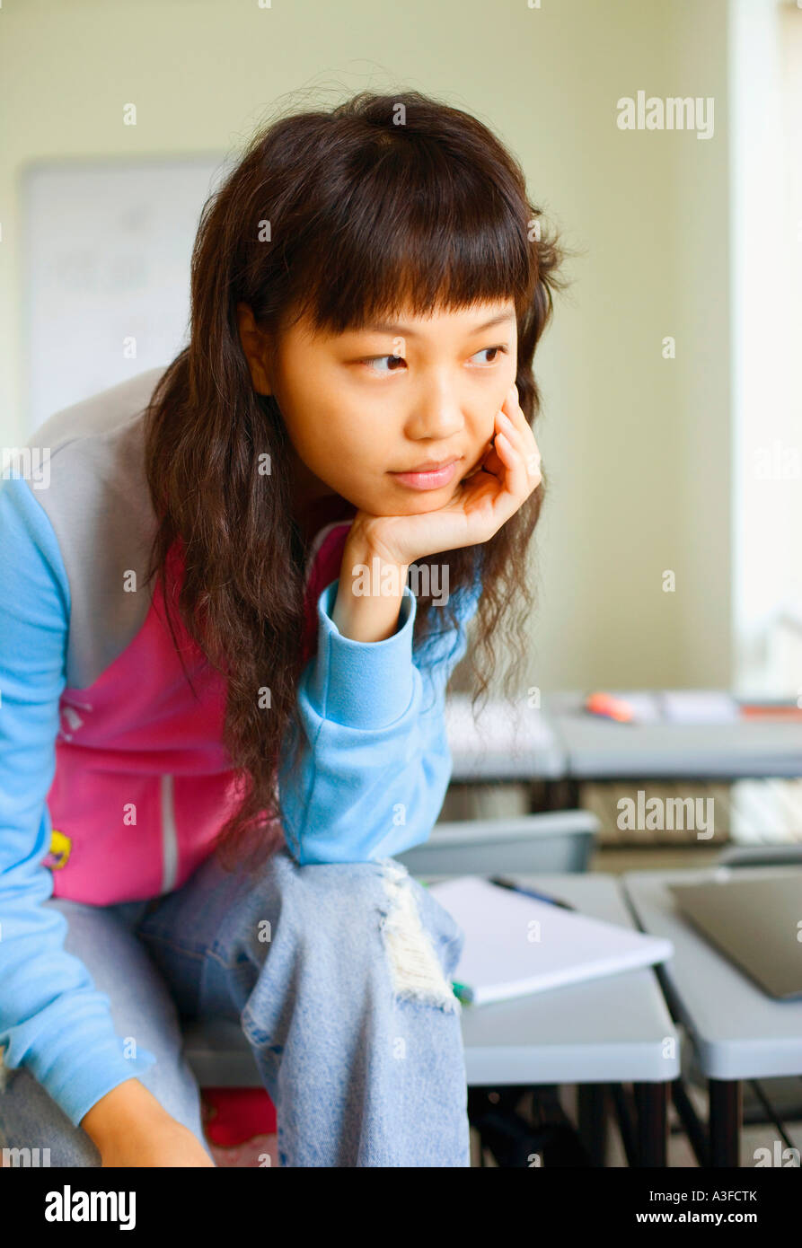 Close-up of a young woman sitting on desk and thinking in the classroom Stock Photo