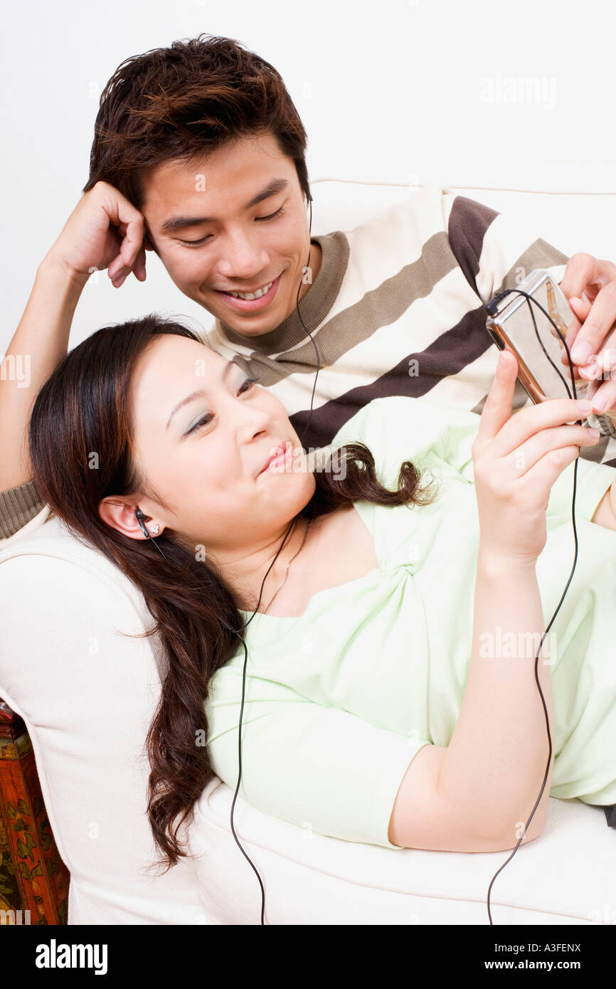 Mid adult man and a young woman lying on a couch and listening to an ...