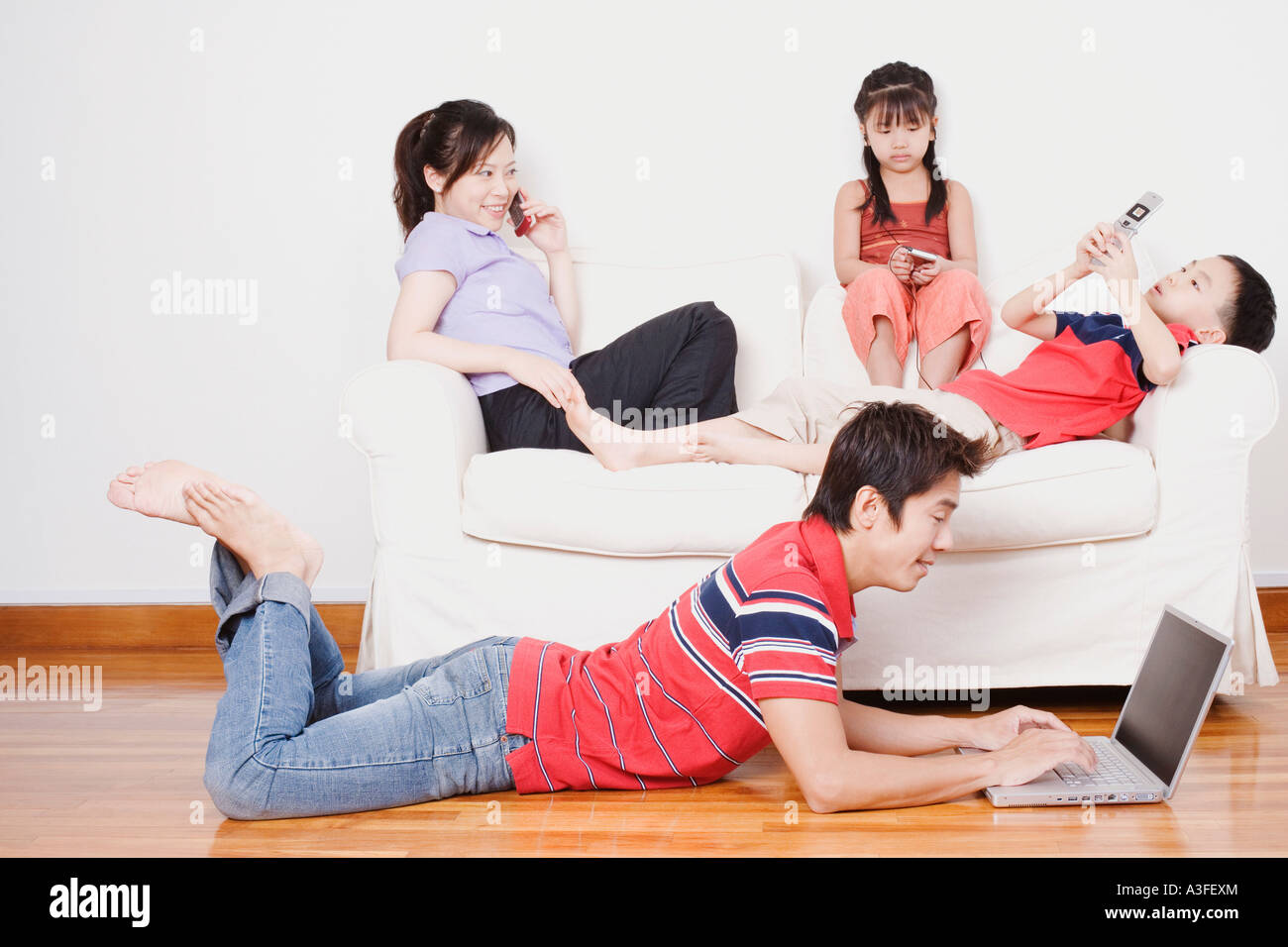 Young woman and her son and daughter sitting on a couch with a mid adult man lying on the floor with a laptop Stock Photo