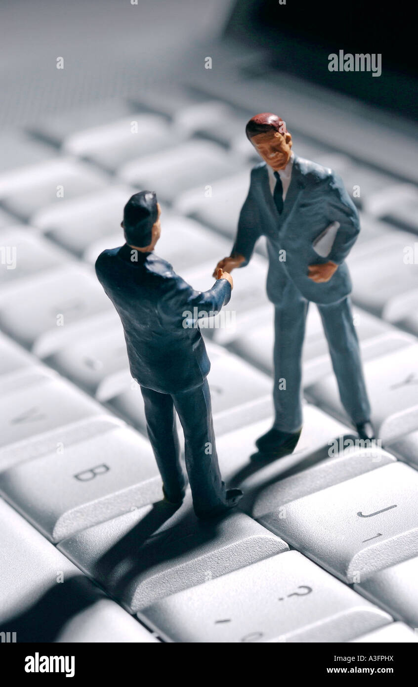 Business meeting online, two businessmen figures shaking hands on a computer keyboard Stock Photo