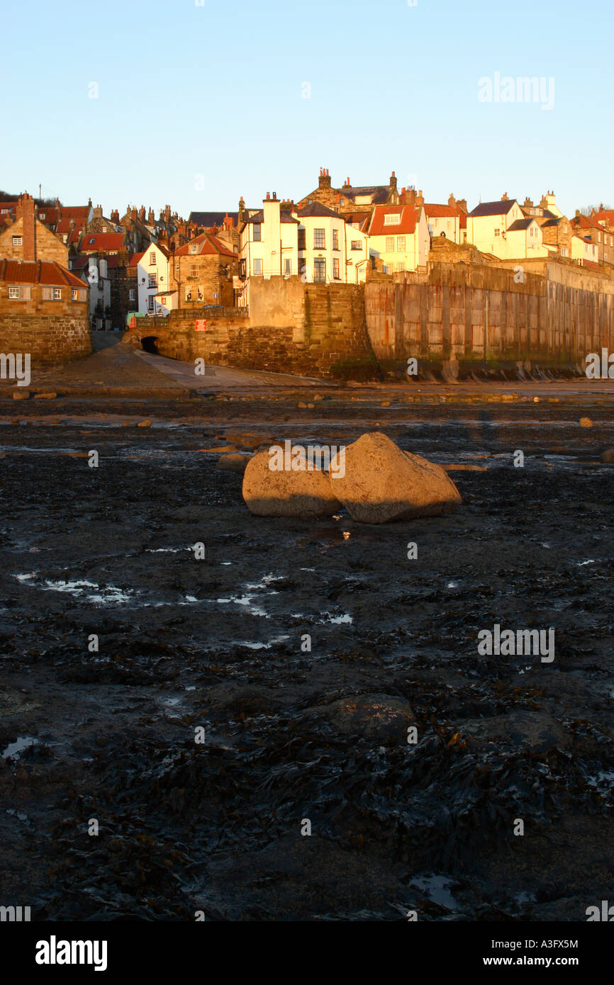 Fishing village of Robin Hoods Bay in North Yorkshire showing sea wall when tide is out with wave worn boulders in foreground at Stock Photo