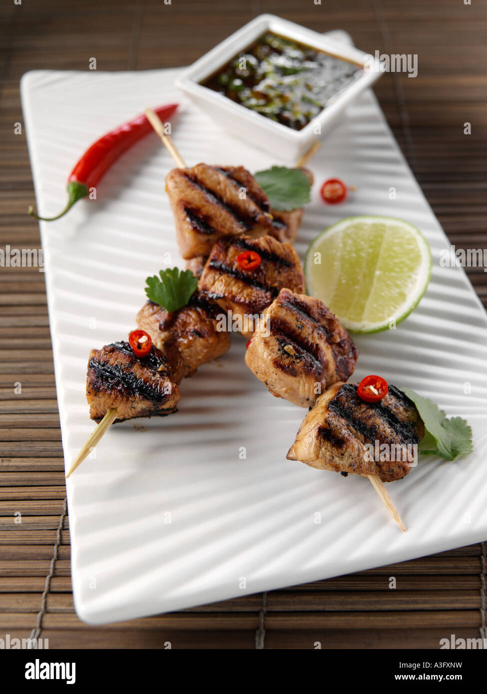 Two Thai chicken kebabs on skewers with dipping sauce editorial food