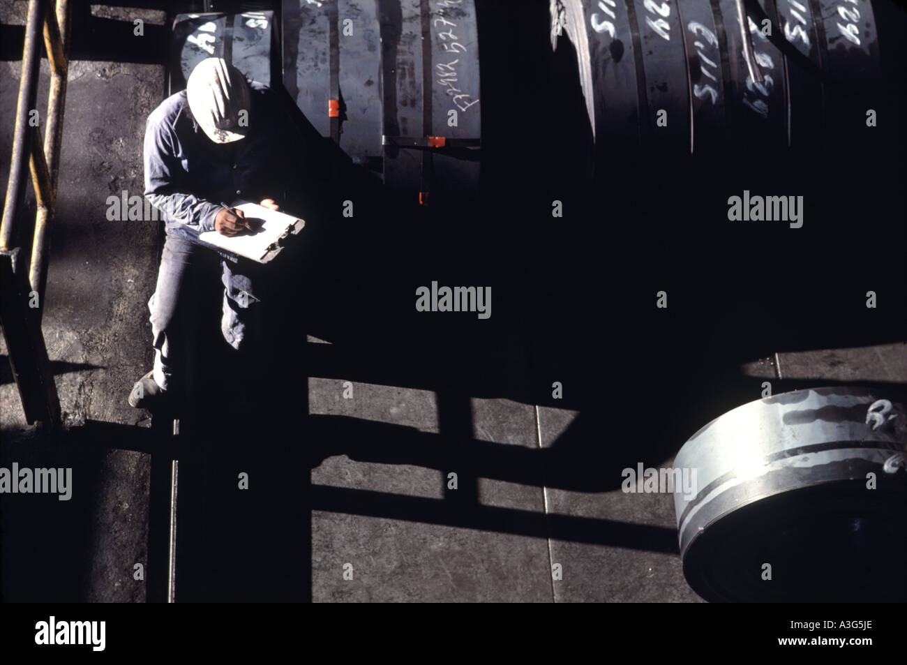 Overhead view of engineer in a white hard hat sitting down to take notes on an offshore oil drilling platform. Stock Photo