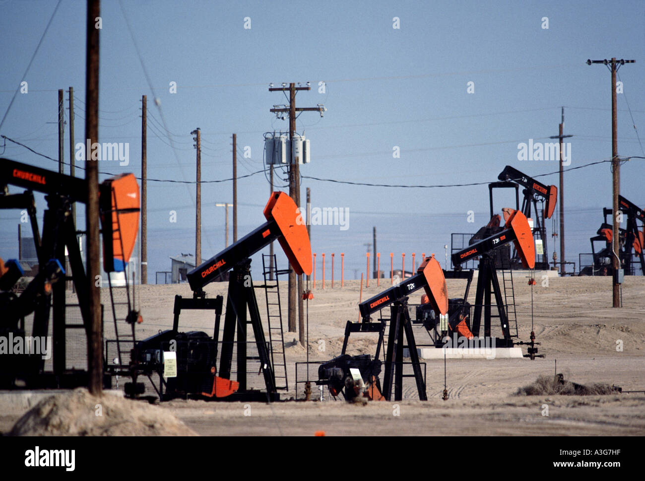 Configuration of  7 orange and black oil extrusion pumps vigorously operating in the parched desert under multiple power lines Stock Photo