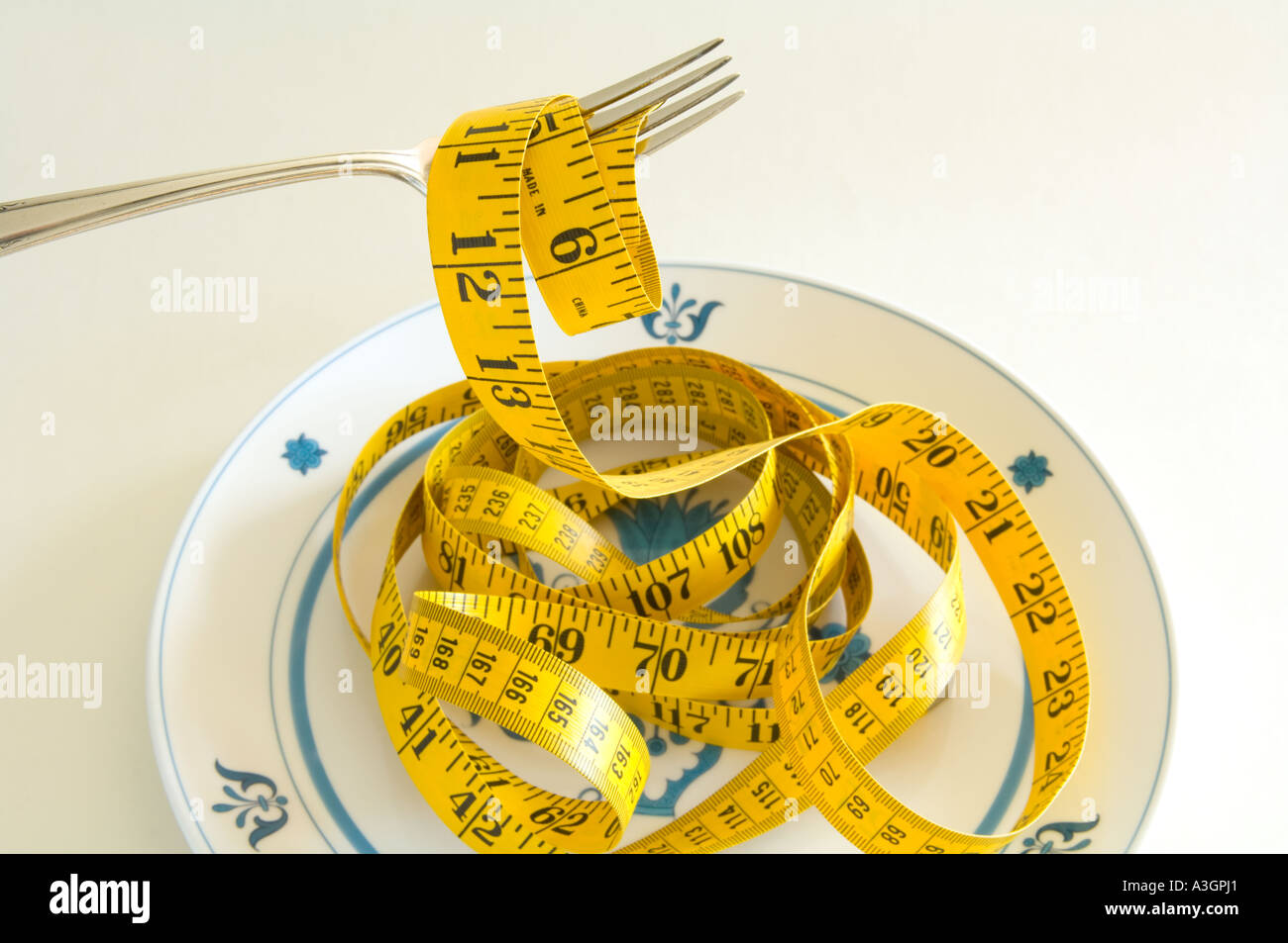 conceptual view of a tape measure displayed on a dinner plate with a fork illustrating gluttony Stock Photo