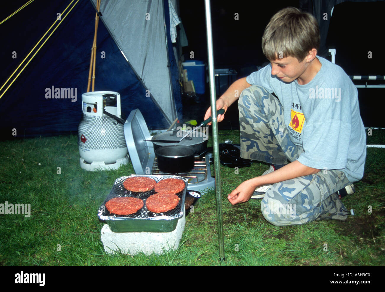boy aged 10 cooking burgers over a BBQ Camping holiday Cornwall
