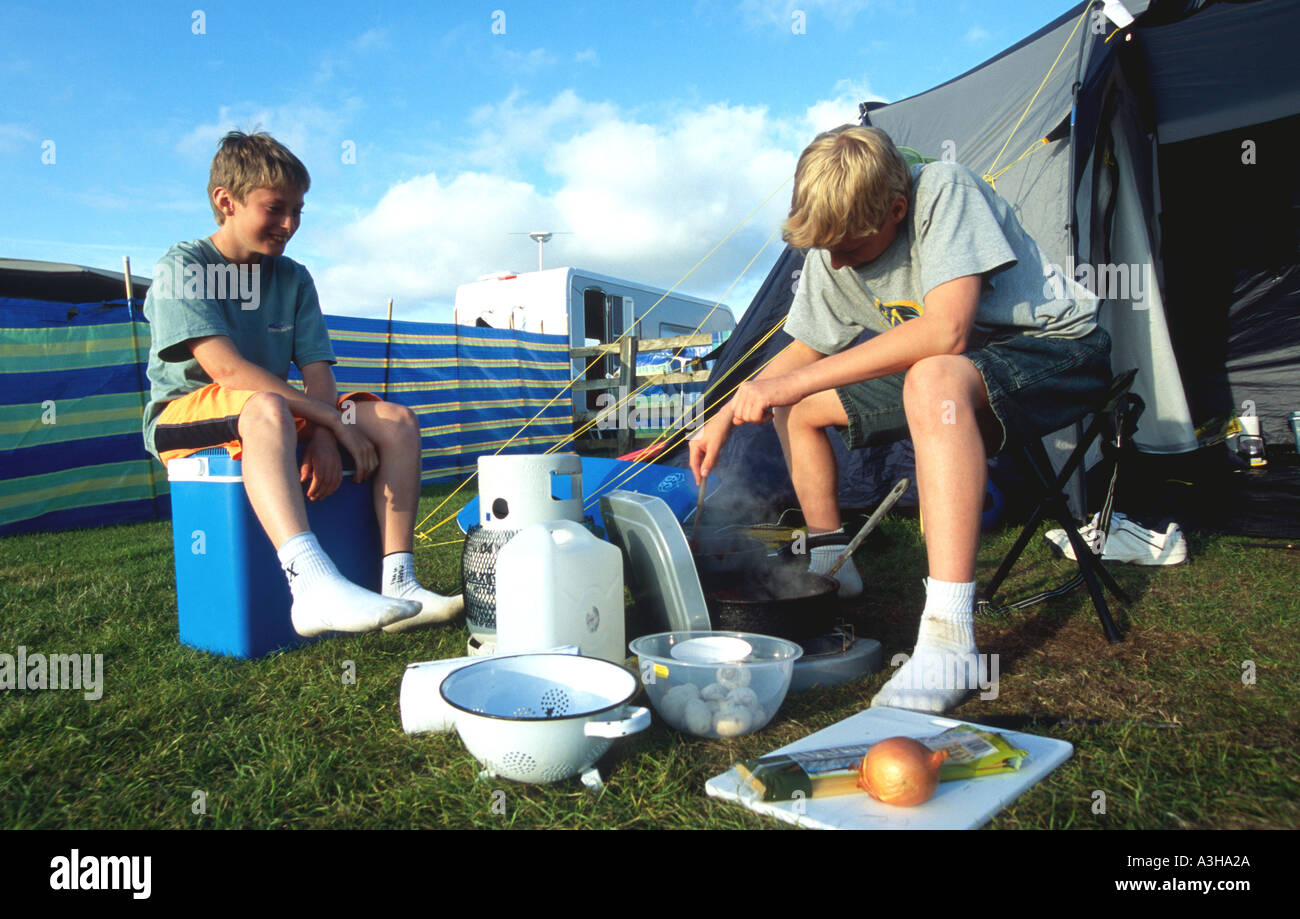 Two boys cooking on a camping holiday Polzeath North Cornwall coast England Britain UK Stock