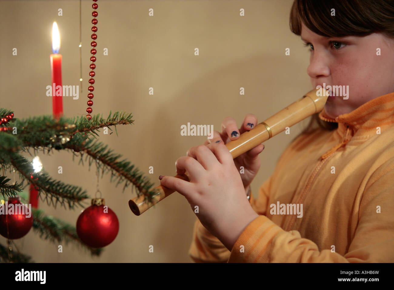 young girl playing the recorder in front of a Christmas Tree Stock Photo