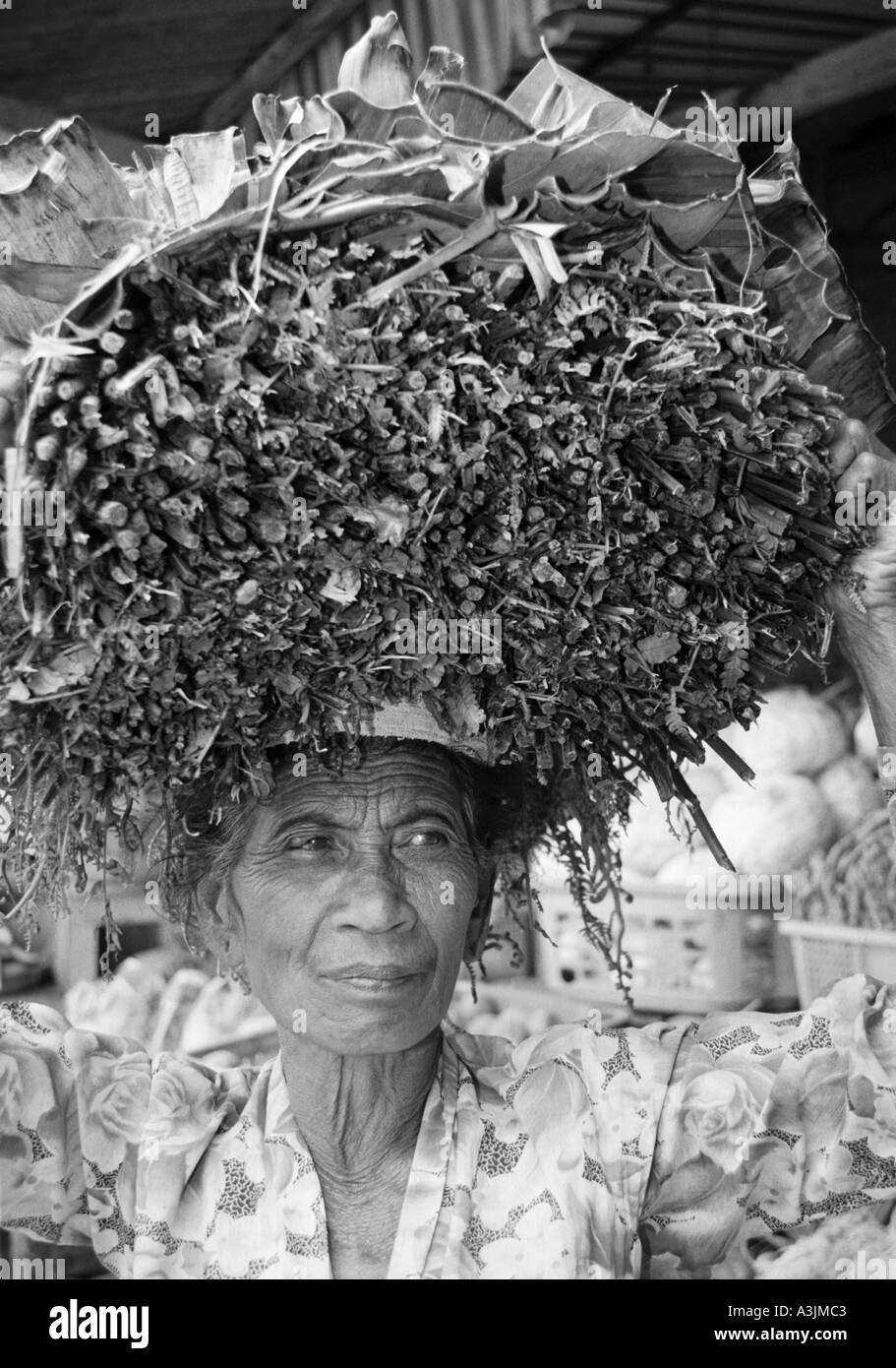 elderly local woman with bundle of leaves and sticks on her head at kandikuning market bali indonesia Stock Photo