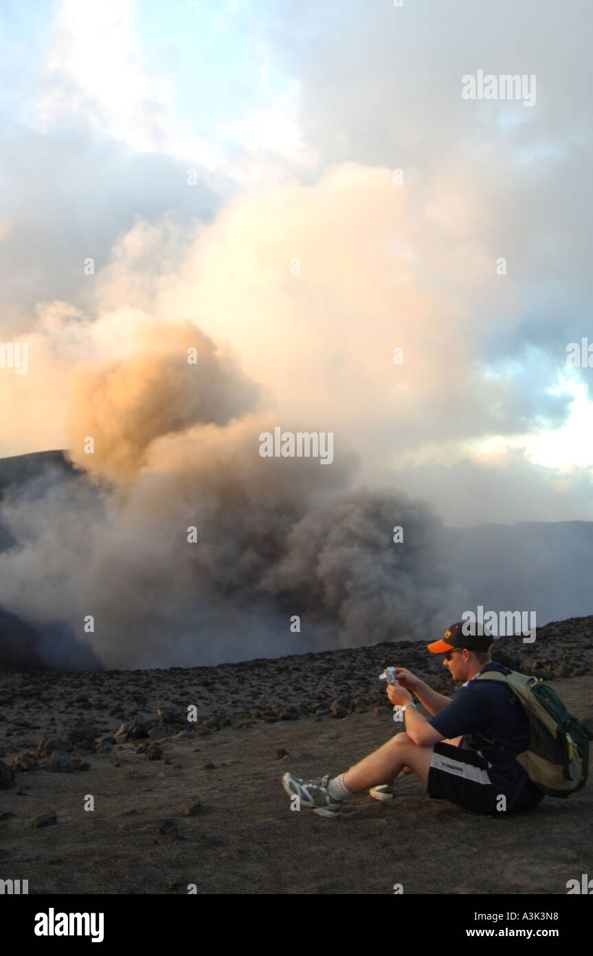 A tourist reviews pictures on his digital camera while Mount Yasur volcano rumbles in the background on Tanna island in Vanuatu Stock Photo