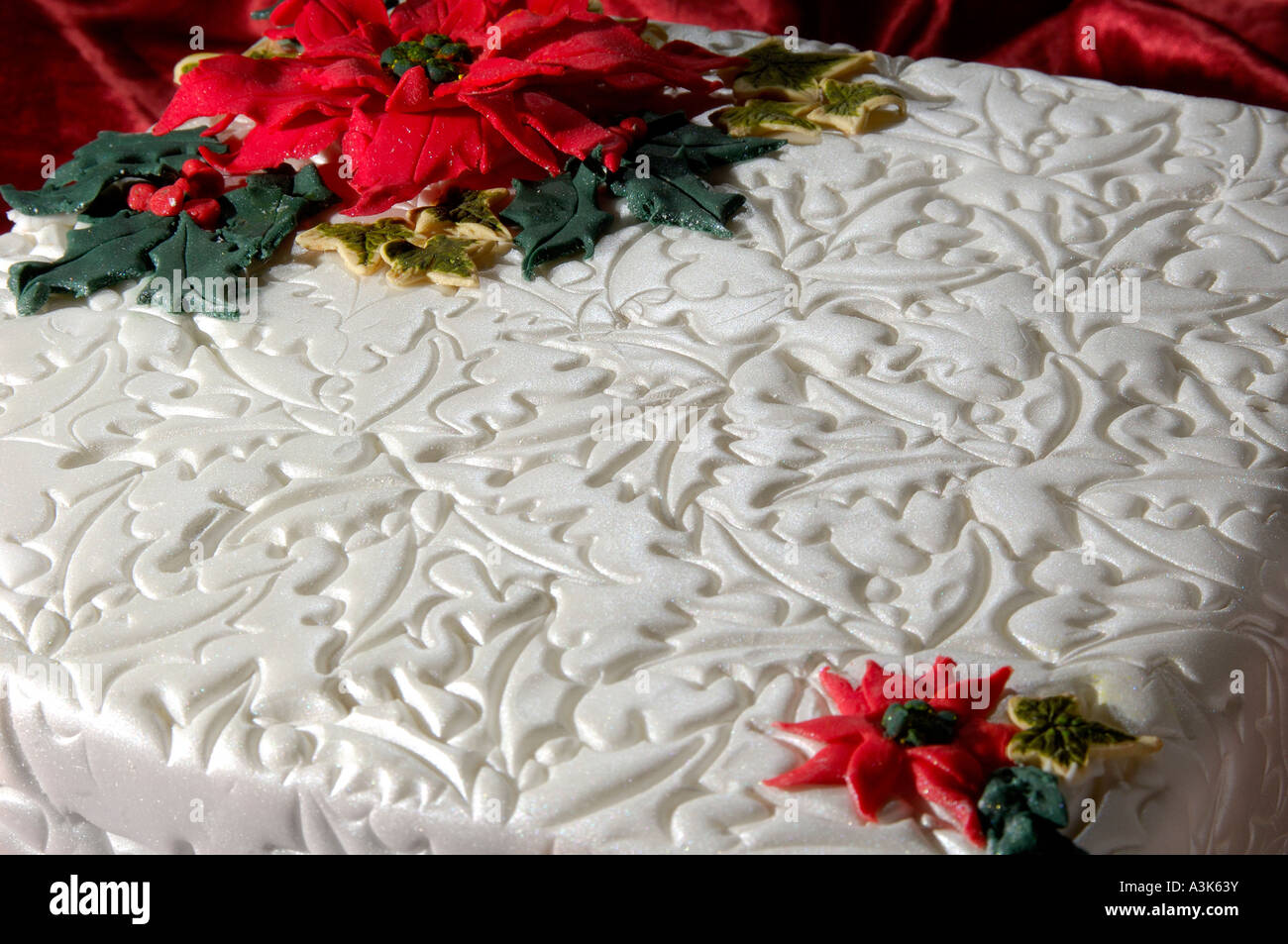 Beautifully decorated iced Christmas fruit cake with embossed holly leaves and red poinsettia flowers made from icing Stock Photo