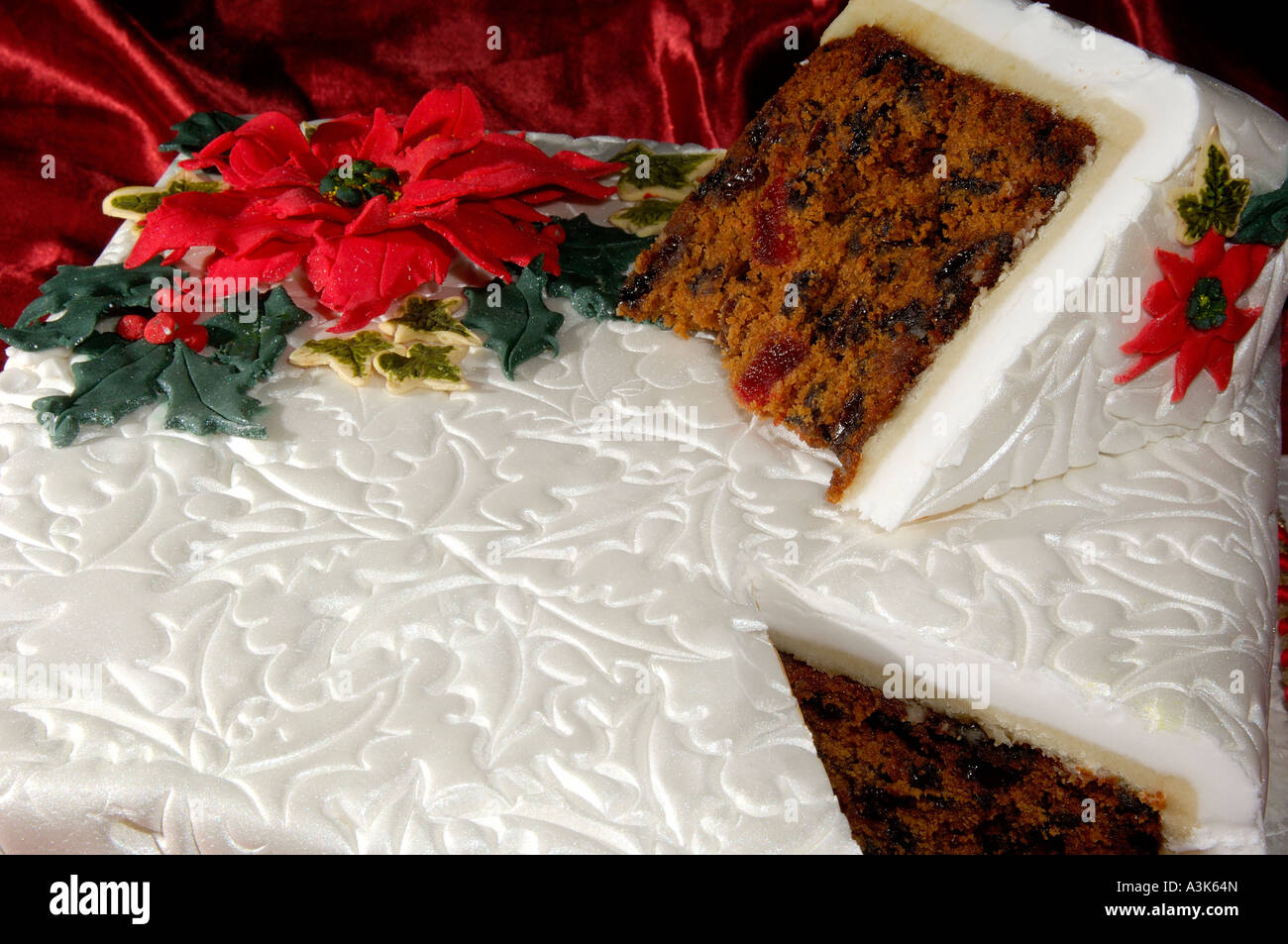 Beautifully decorated iced Christmas fruit cake with embossed holly leaves and red poinsettia flowers made from icing Stock Photo