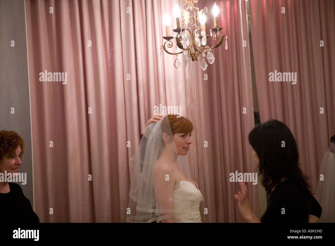 A young woman looks at herself in a mirror as she tries on a white wedding dress in a store in New York USA January 2006 Stock Photo