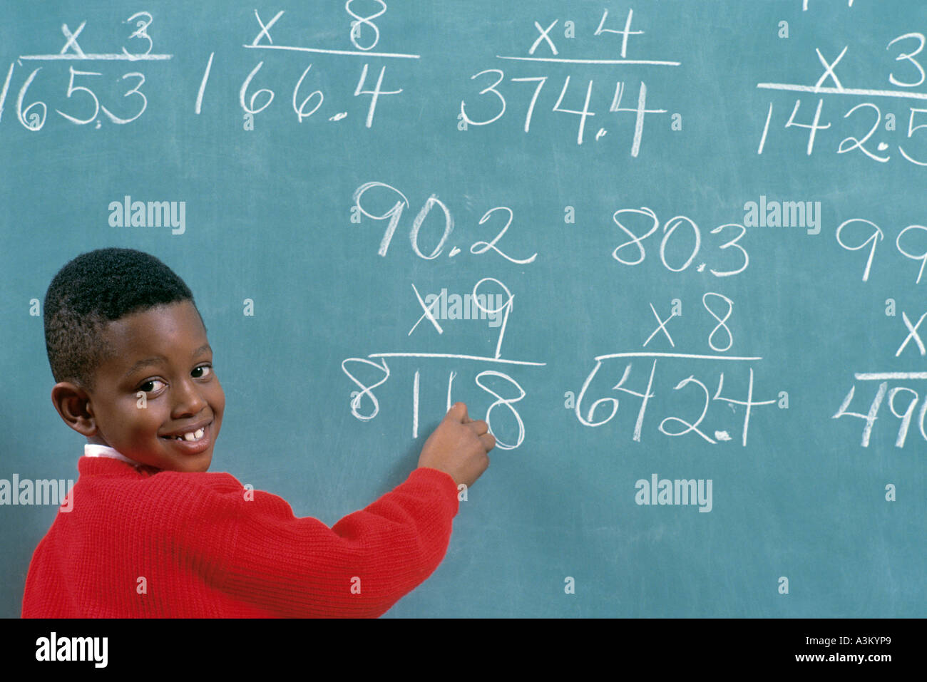 African American male student solving math problems on chalk board in elementary school class Stock Photo