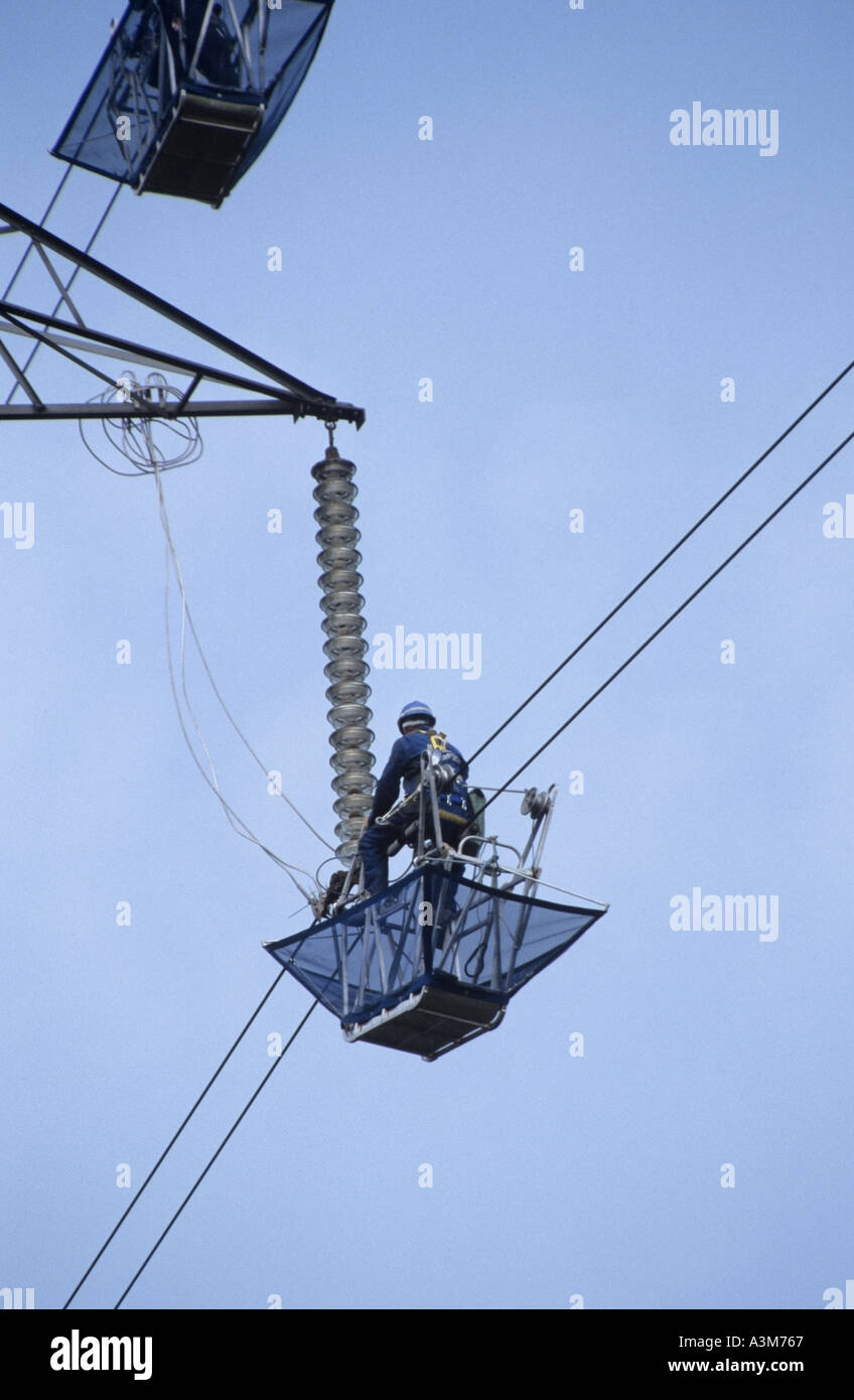 Haltwhistle overhead high voltage electricity power line maintenance work men in cradles running on cables Stock Photo