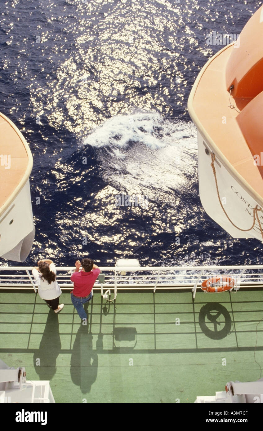 Aboard cruise ship ocean liner on a Mediterranean cruise couple beside deck rails between lifeboats looking out to sea Stock Photo