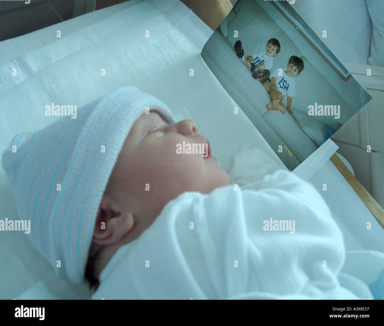 Newborn baby sleeping in hospital crib with brother s pictures beside