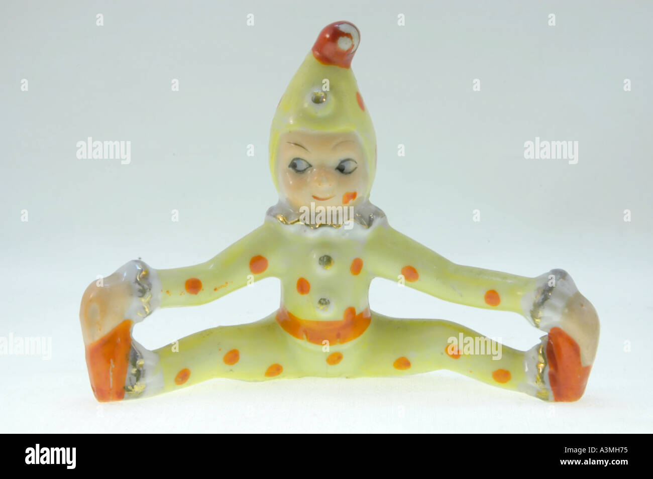 Antique ceramic pixie dressed as a clown sitting down or jumping and touching his feet Stock Photo