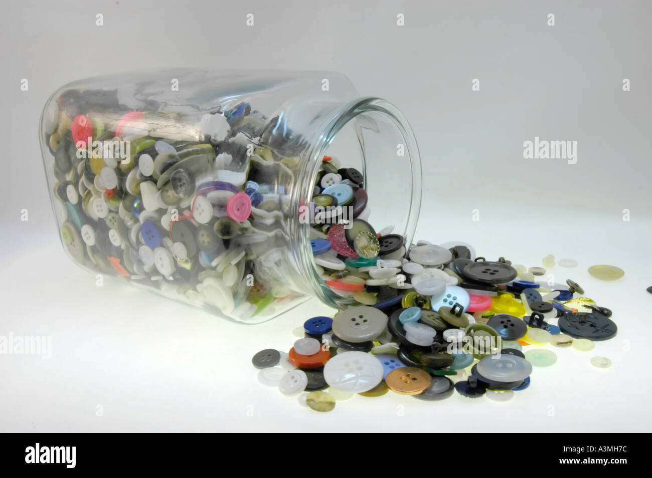 Clear glass jar turned over on the side with buttons of multiple sizes and colors spilled out Stock Photo
