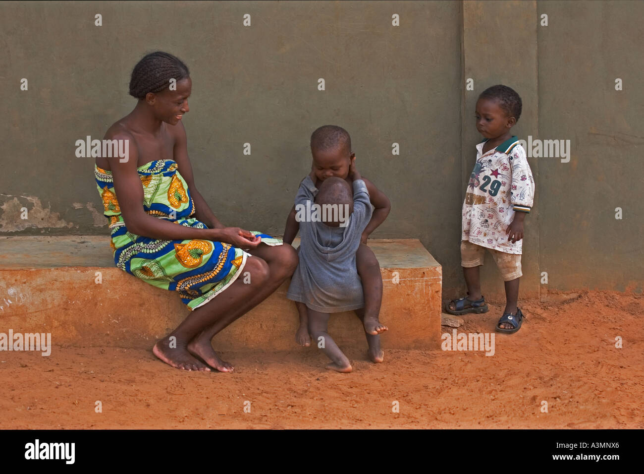 Happy African mother from Ghana and baby toddler hugging slightly older brother with another brother looking on Stock Photo