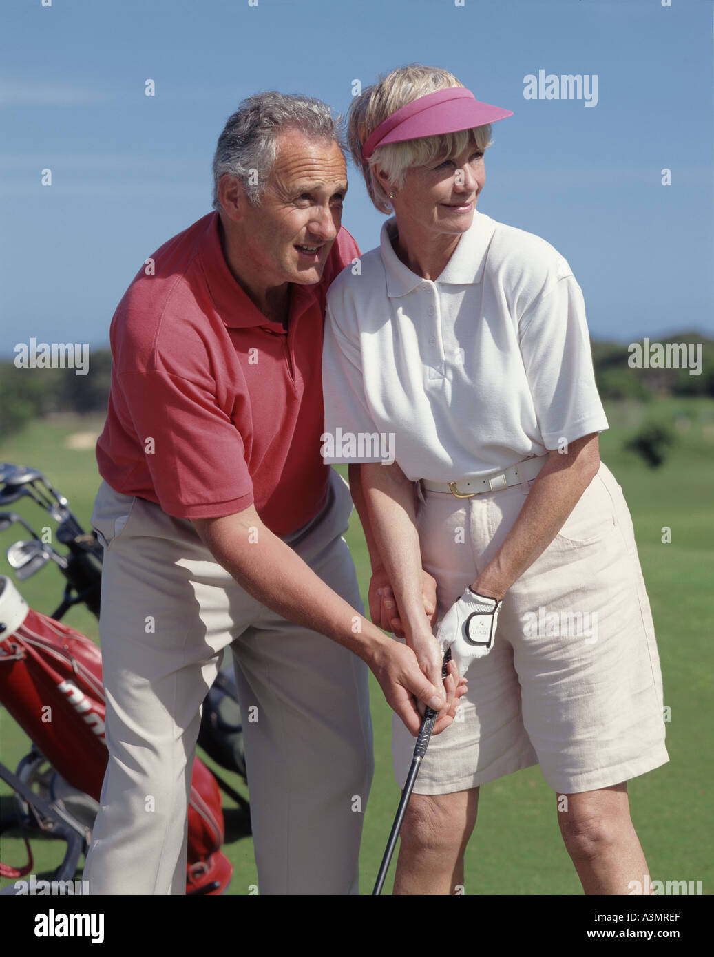 retired couple, with man helping woman with golf swing Stock Photo