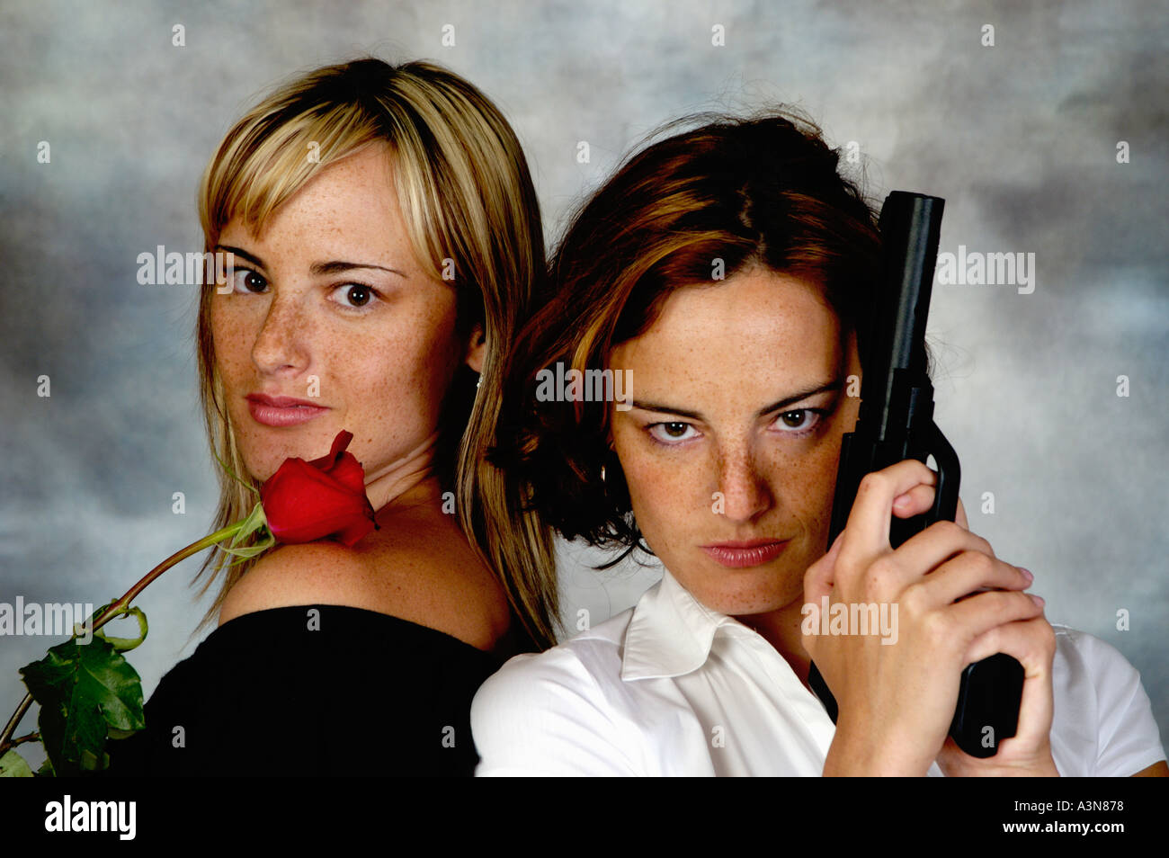 Twin sisters posing with a gun and a rose Stock Photo