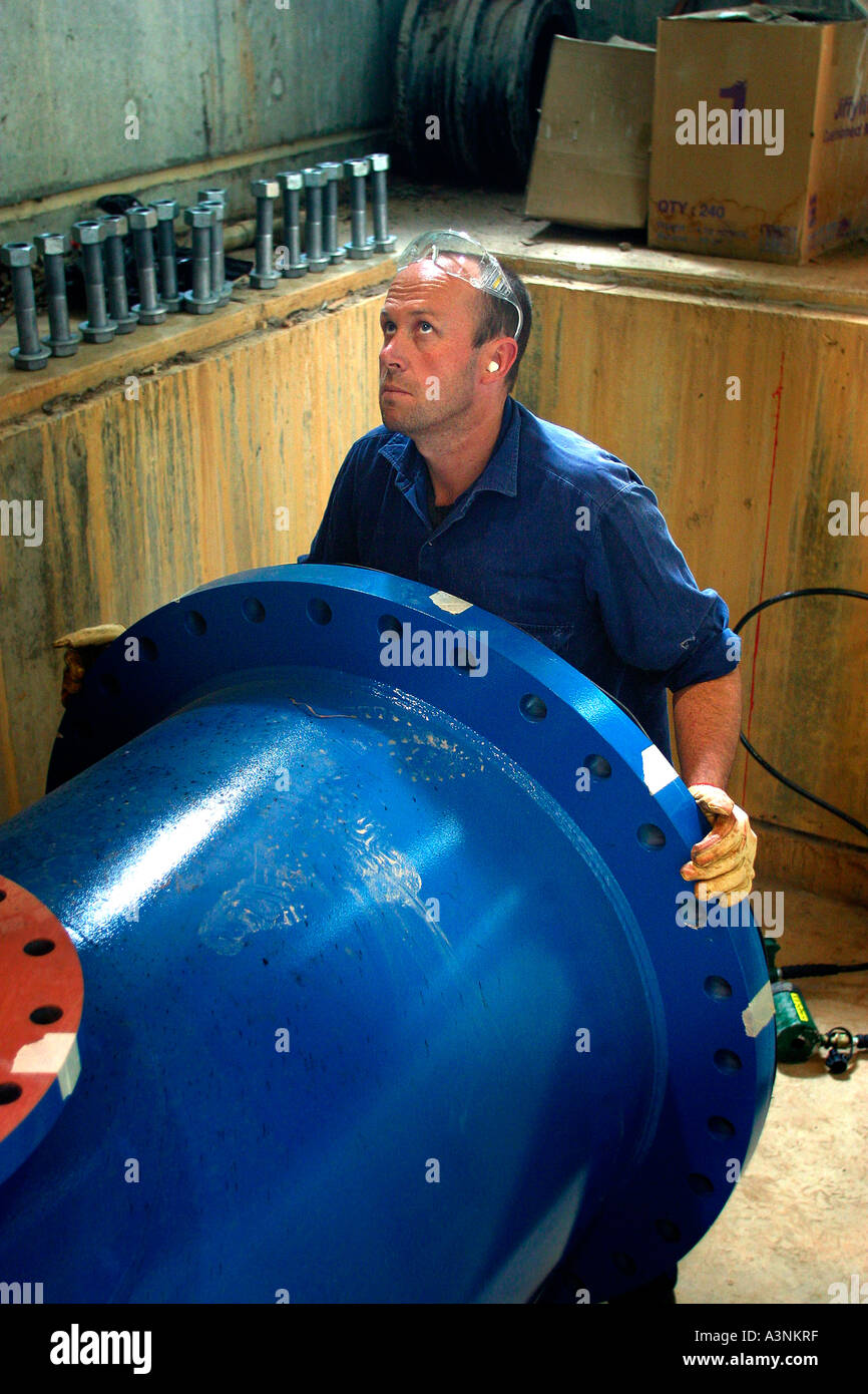 Water supply construction A worker makes adjustments to the position of a large diameter water pipe prior to connection Stock Photo