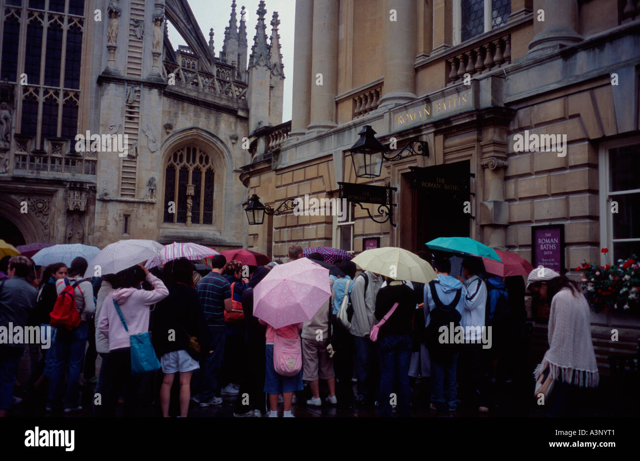 Tour party in the rain with umbrellas, queuing to get into the Roman Baths Bath Spa, Somerset, England UK Stock Photo