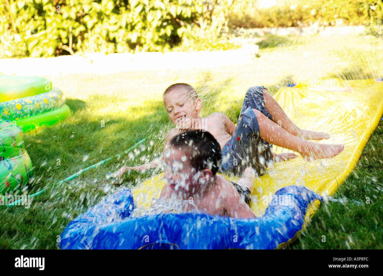 5 and 3 year old brothers playing on water slide Stock Photo