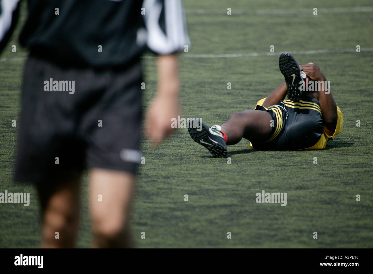 black injured football player rolls on the ground holding his leg Stock Photo