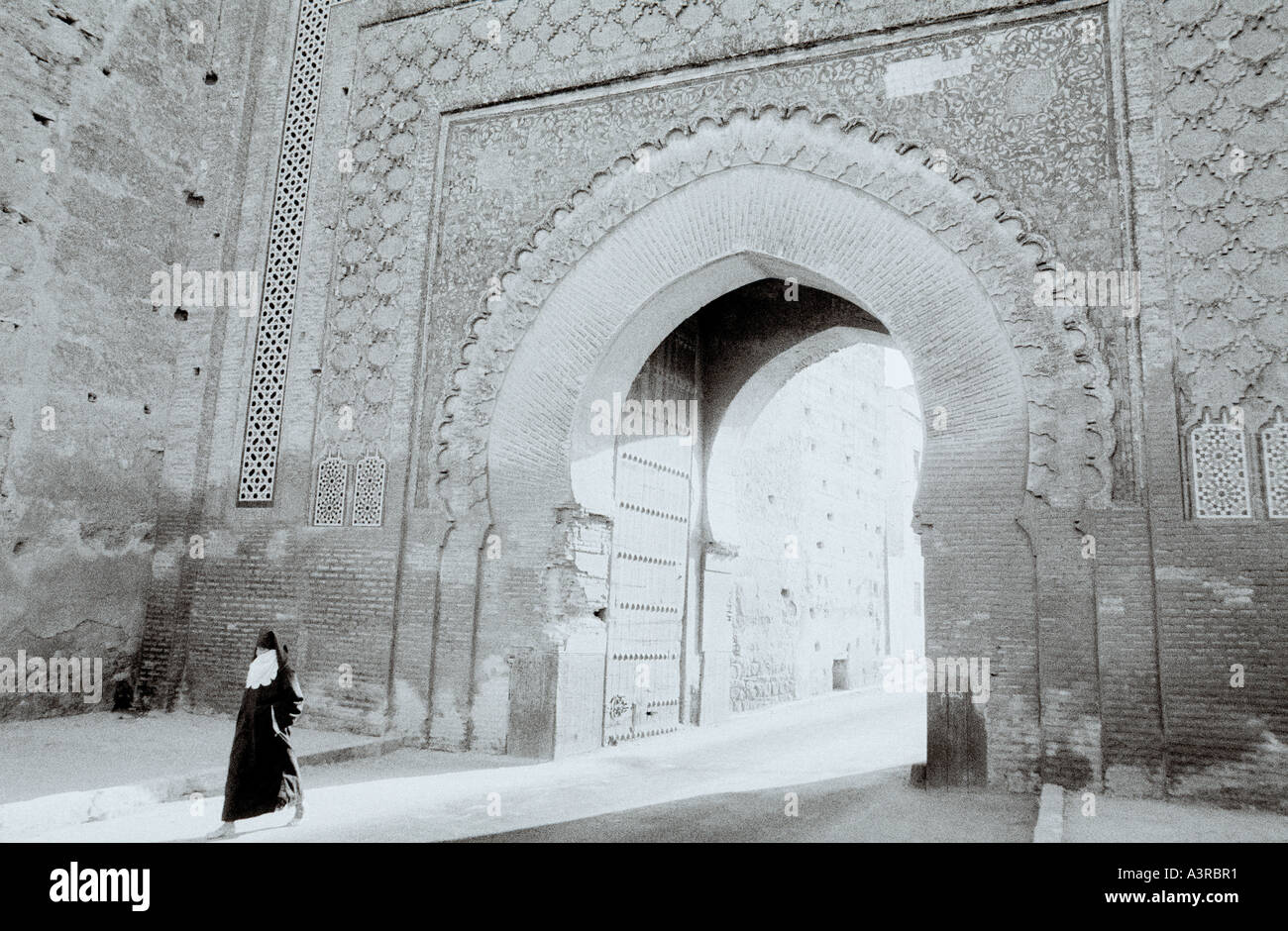 A woman in yashmak face veil walks through the Bab Mansour Gate in the Meknes Casbah Medina in Morocco in the Maghreb in North Africa Sahara. Travel Stock Photo