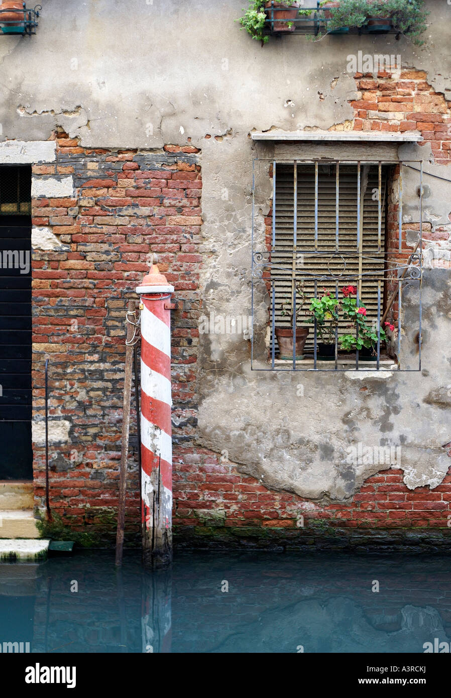 Red and white striped mooring pole on side canal. Venice, Italy Stock Photo
