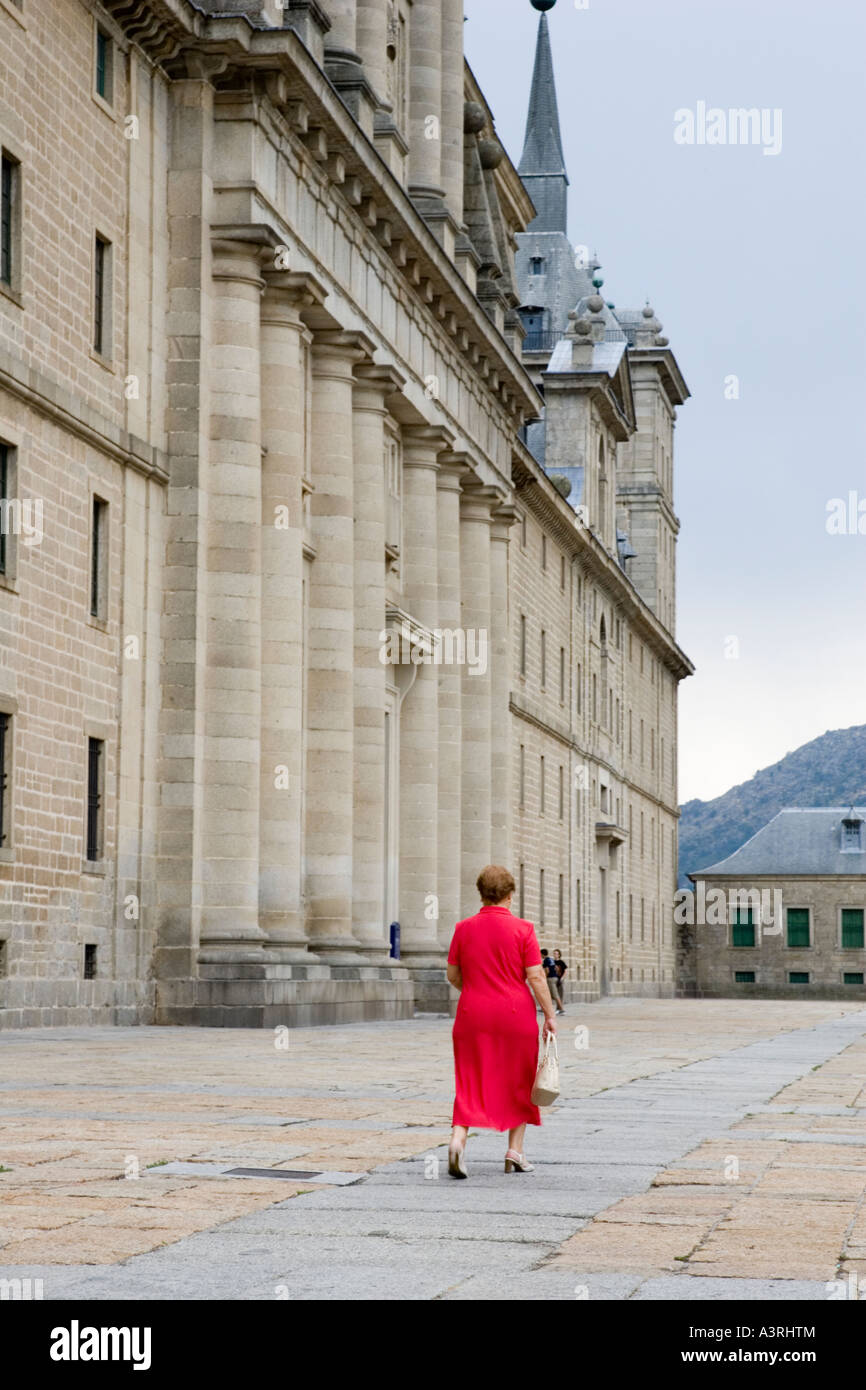 Woman in red walking in front of El Escorial facade, Spain Stock Photo