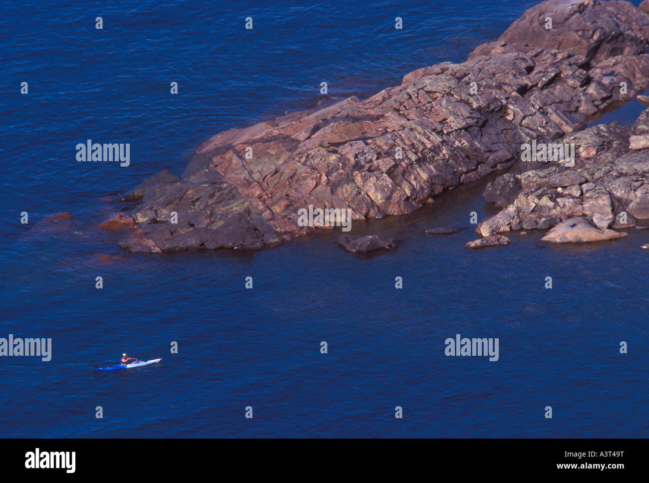 A sea kayaker is seen from above as he paddles near a large granite outcropping on Lake Superior near Marquette Mich Stock Photo