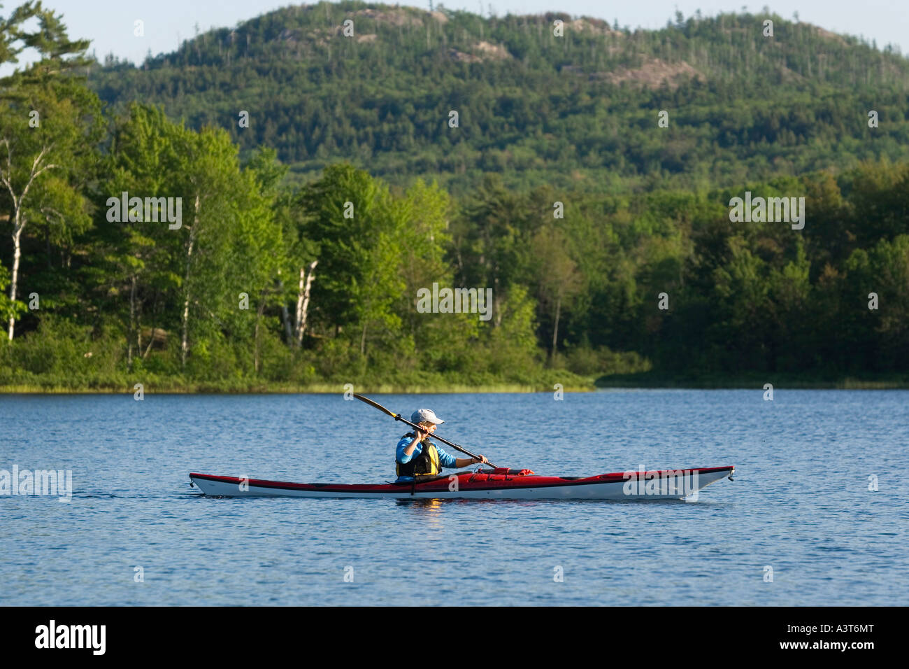 A female sea kayaker paddles a red kayak on Harlow Lake in the Escanaba