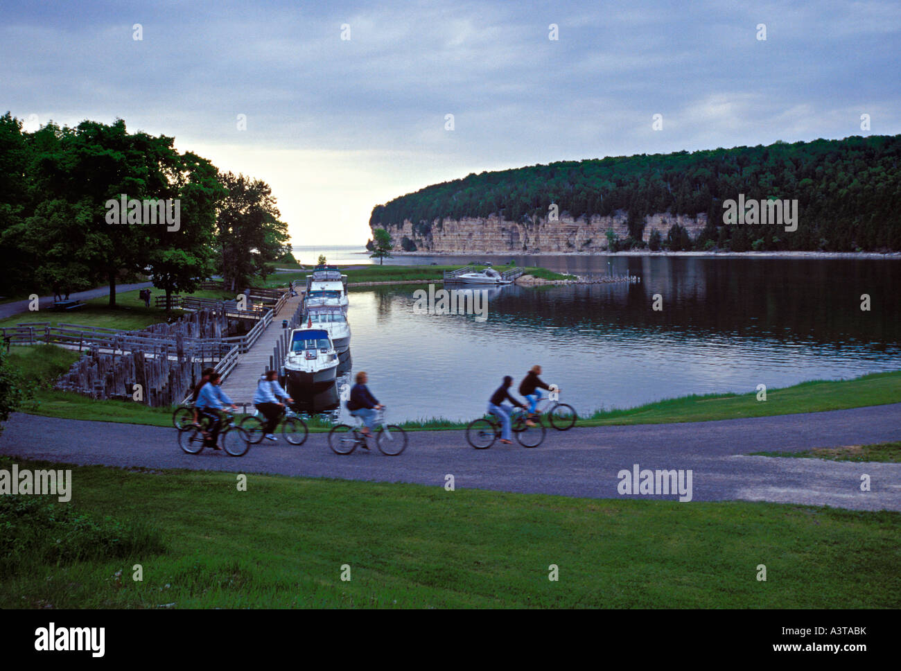 A FAMILY BIKES PAST BOATS DOCKED IN SNAIL SHELL HARBOR AT FAYETTE STATE HISTORIC PARK ON THE GARDEN PENINSULA Stock Photo