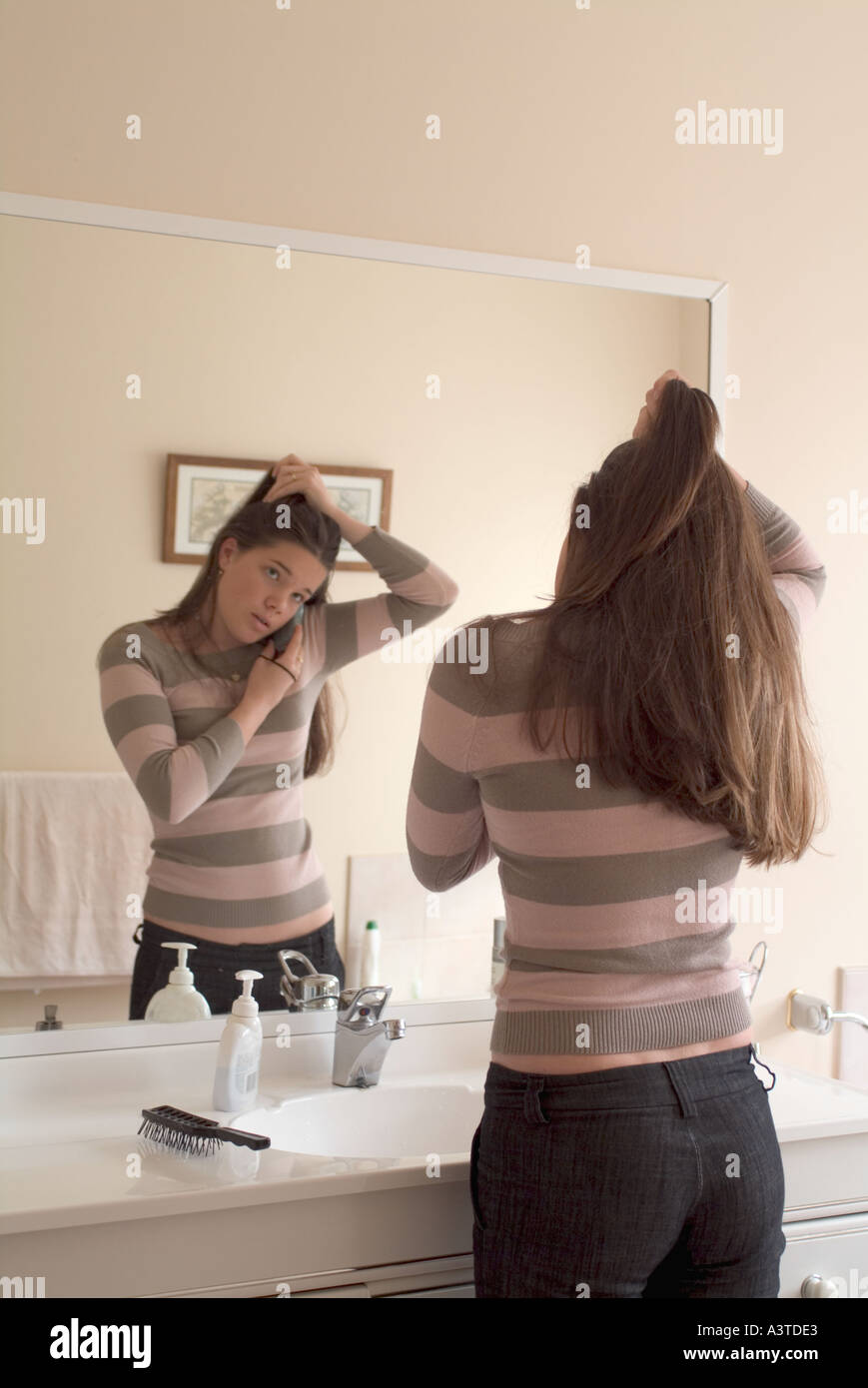 Teenage girl in from of a mirror doing her hair and answering her ...