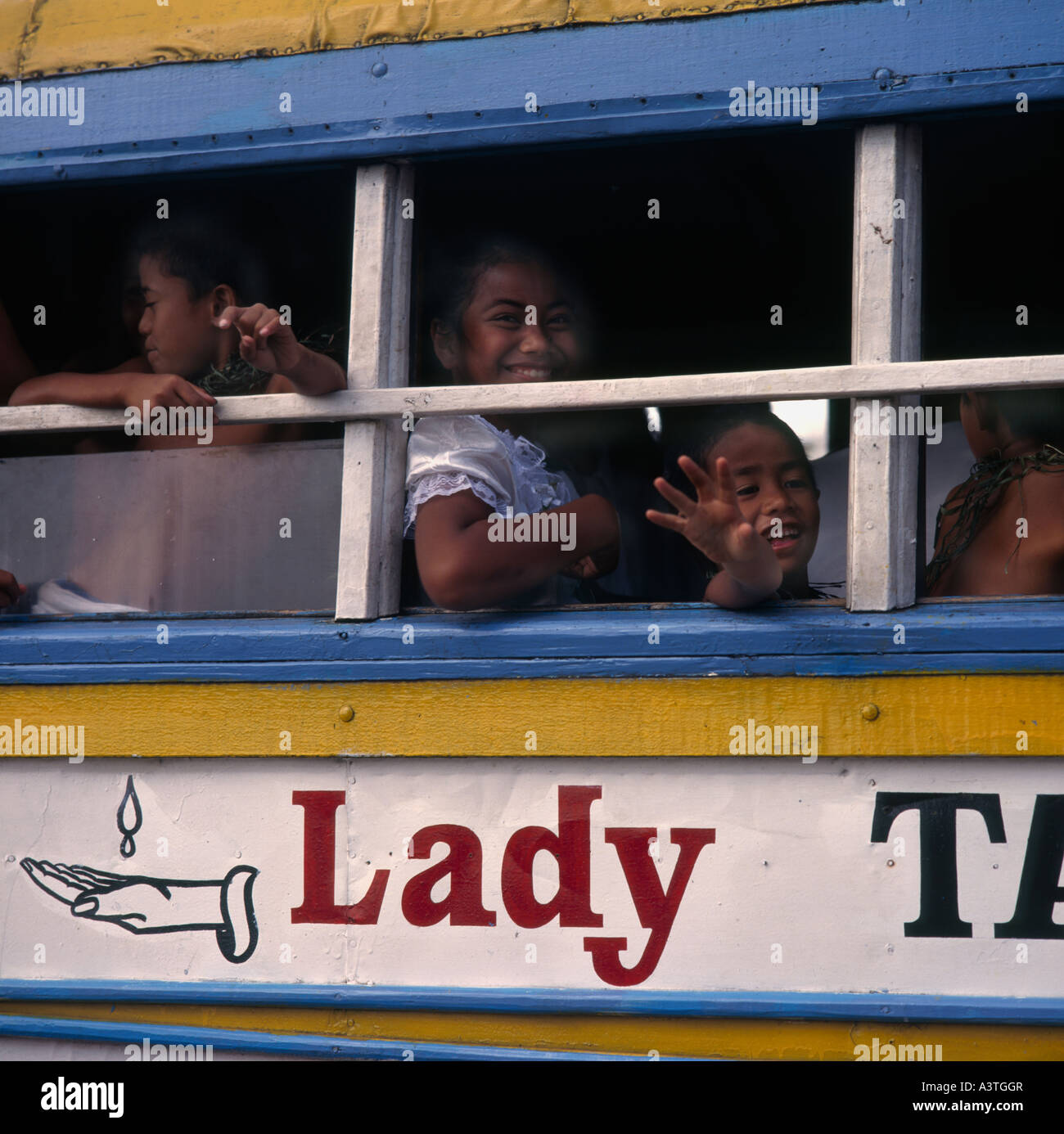 Local style Samoan Church bus in colourful yellow white and blue with girls at window in Apia town on Upolu Island Western Samoa Stock Photo