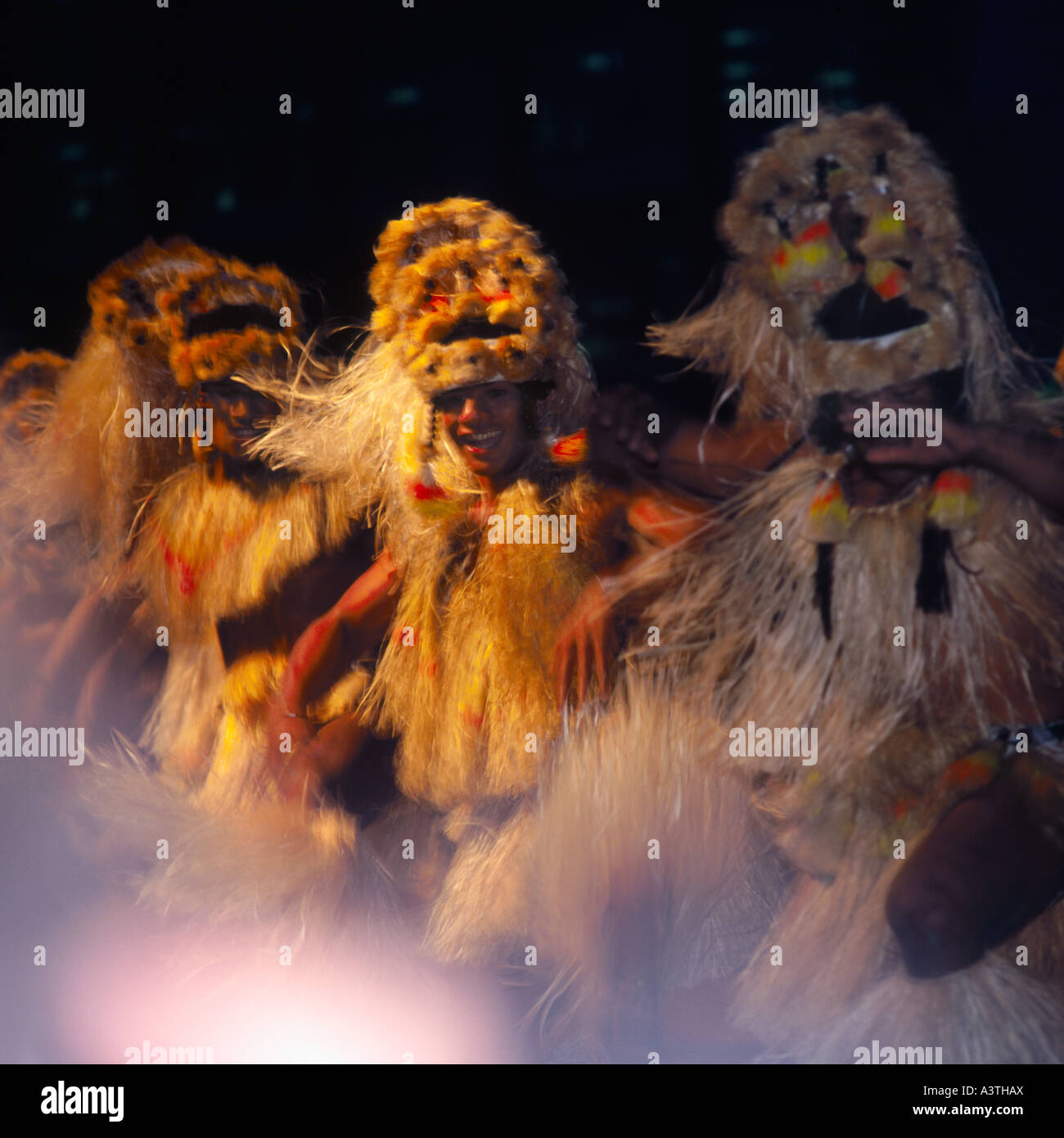Three Tahitian dancers in a line at night in traditional dress of grass skirts tops & headdress at the Festival of Pacific Arts Stock Photo