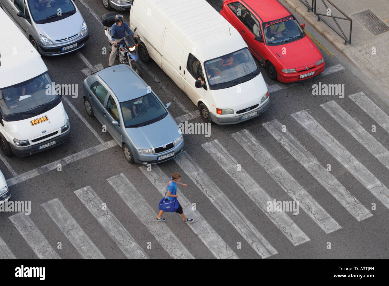 One pedestrian crossing busy road on zebra crossing with car traffic vehicles waiting Stock Photo