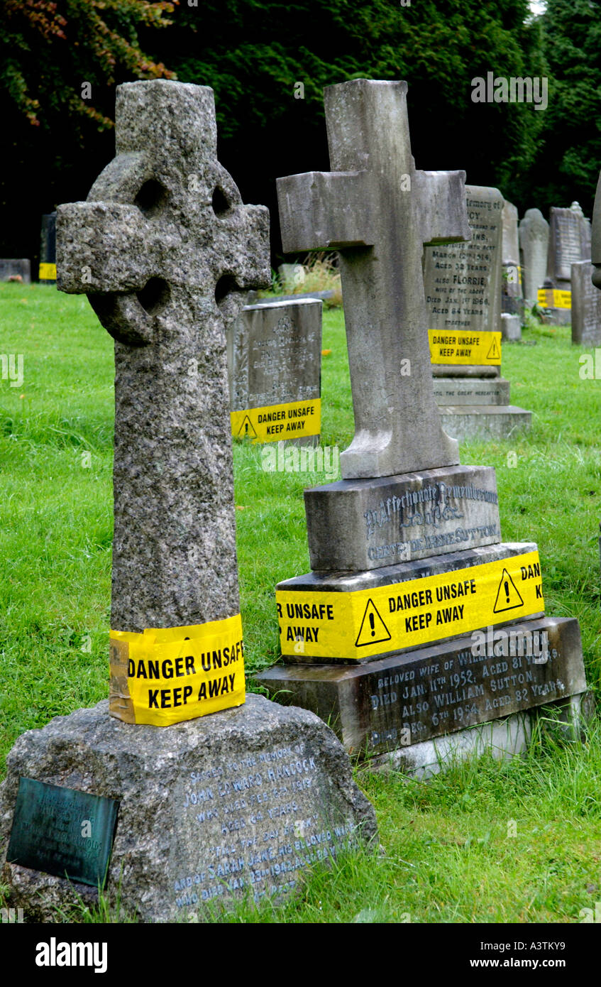 Unsafe headstones with yellow warning notices at a cemetery in Risca South Wales UK Stock Photo