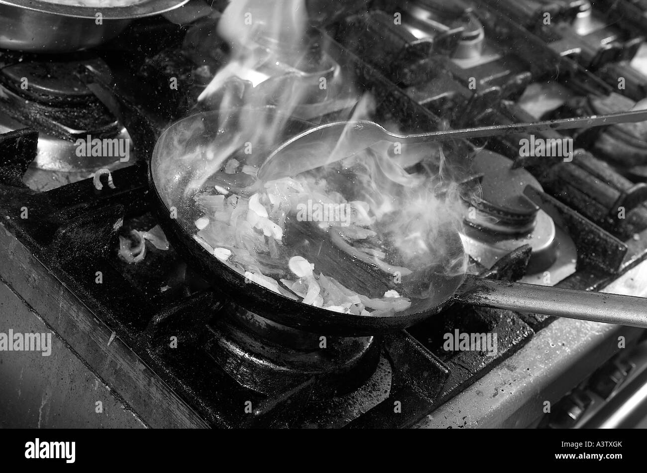 Close up of chef cooking in industrial kitchen adding spice and flames Stock Photo