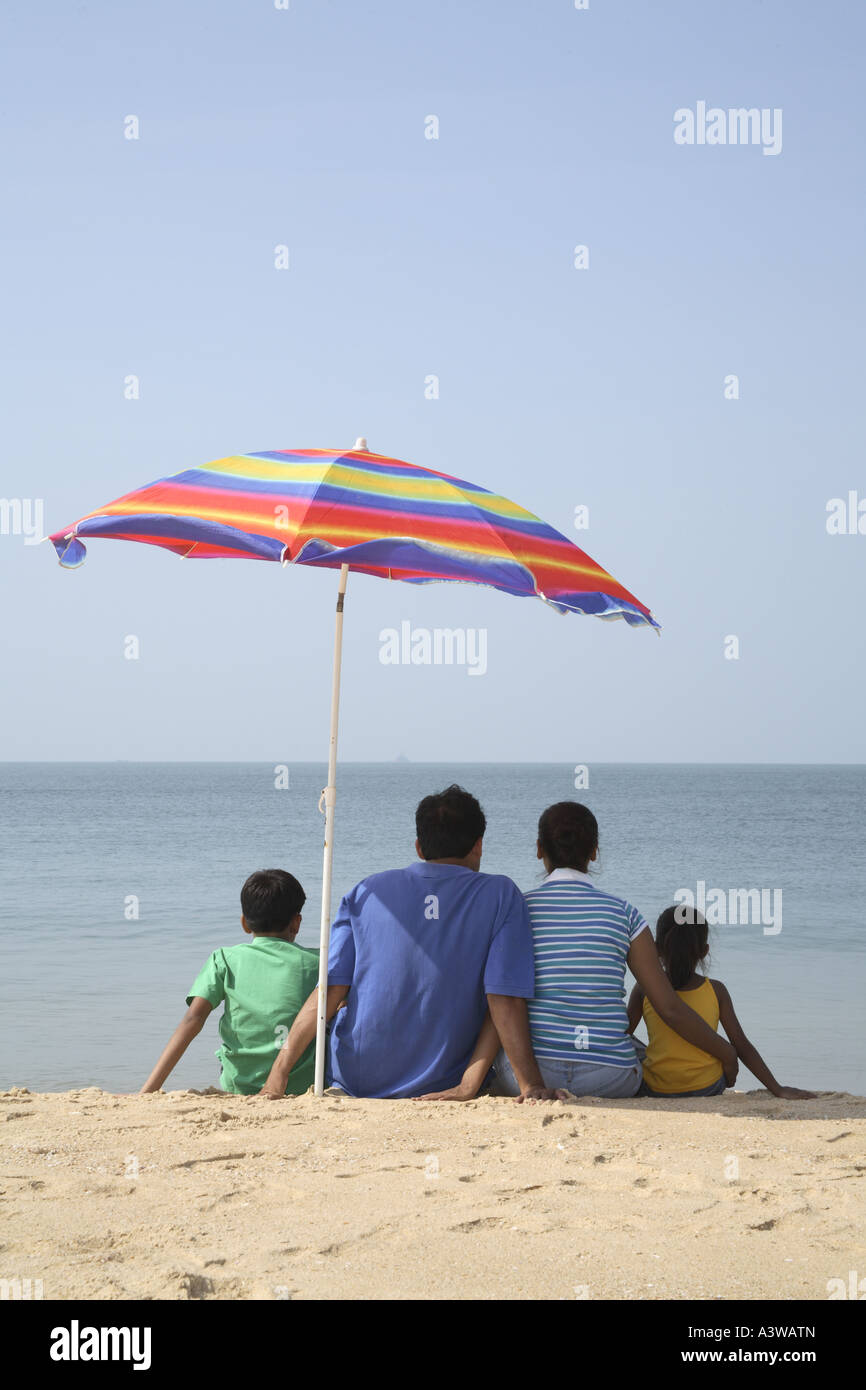 Family Of Four Sitting Below Umbrella On The Beach Lo Ng At The Sea Family Of Four Sitting Below Umbrella On The Beach Lo Ng At The Sea